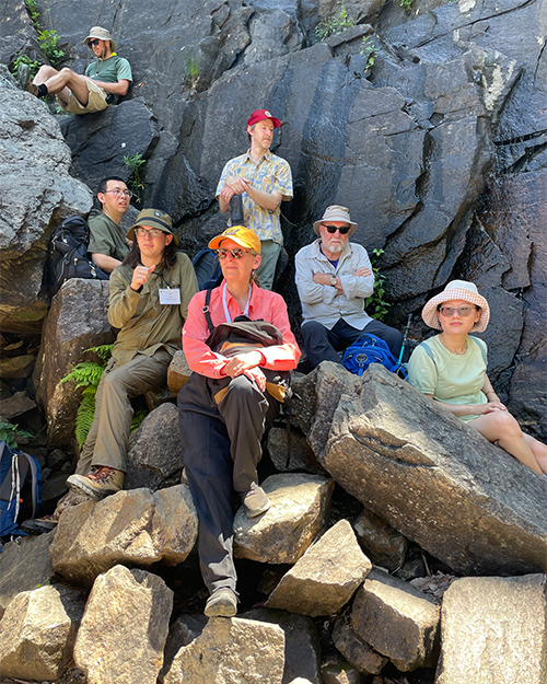Seven people dressed for a hike rest among boulders.