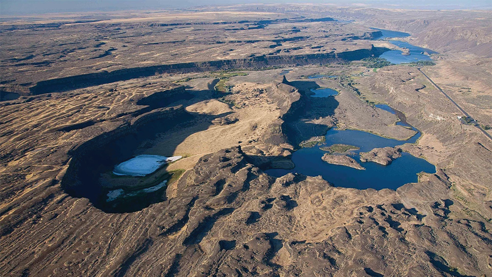 An aerial photograph of an arid landscape sharply eroded by water into buttes and bluffs.