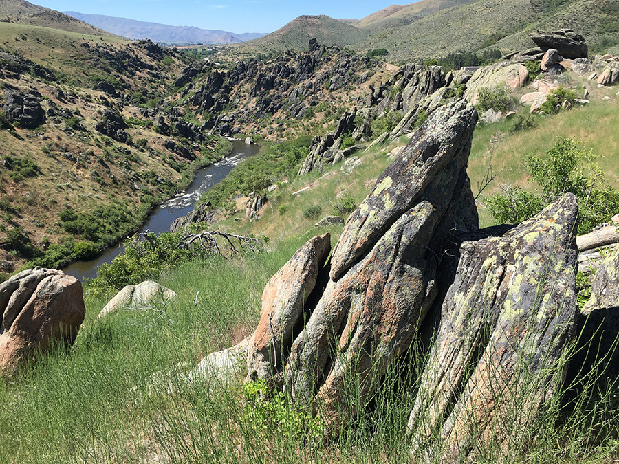 Layered rocks protrude from a steep grassy canyon at a nearly vertical angle.