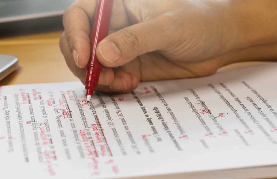 A close-up shot of a person holding a red pen and marking up a document.