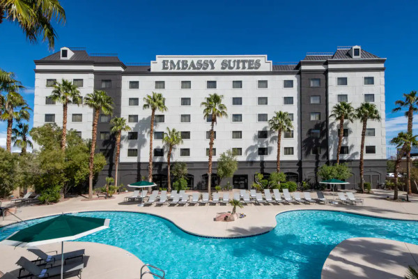 Exterior of Embassy Suites Las Vegas under a clear blue sky with a pool and palm trees in the foreground.