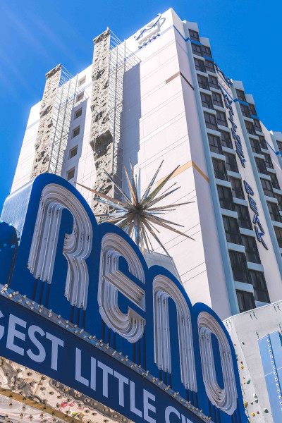 A tall, light colored building with blue accents rises into the sky with a sign reading 'Whitney Peak' on the side and another reading 'Reno' near the base.