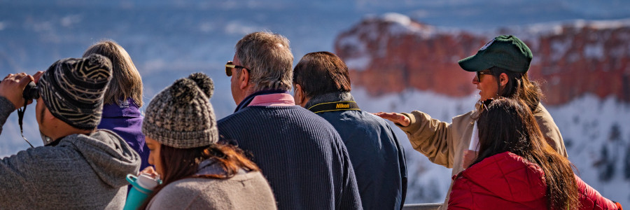 A program participant speaks to a group of people overlooking a snowy canyon.
