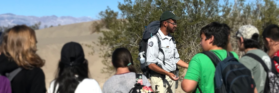 A program participant speaks to a group of young people in a desert setting.