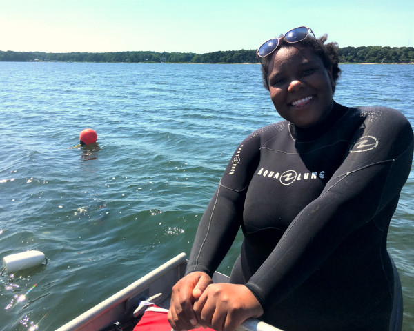 A woman in a wet suit smiles with the ocean and buoys in the background.