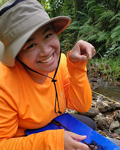 A researcher holds up a small insect-like creature caught from a stream.