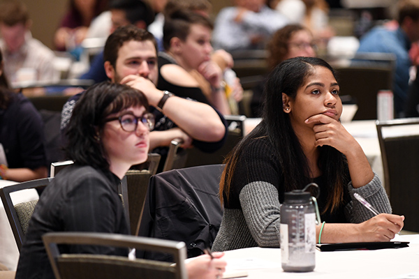 Young people in an audience listen to a speaker.