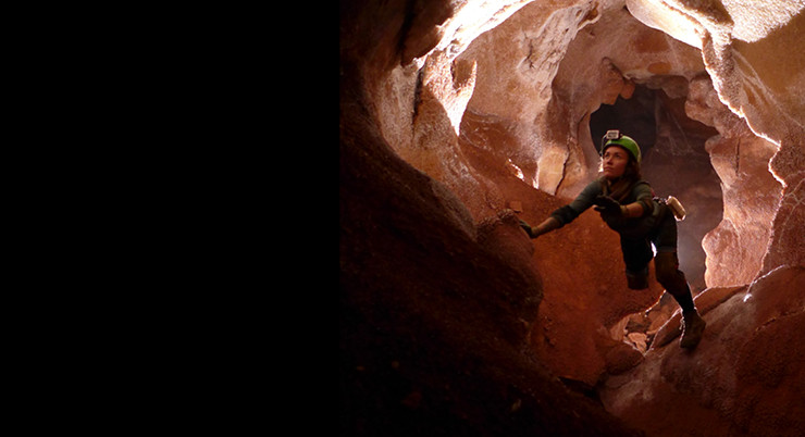 A woman moves through a cave wearing protective equipment.