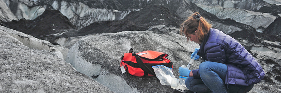 A young woman makes observations on a blackened snowfield.