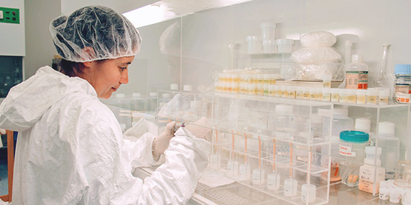 A young woman holds an instrument and notes in the field and smiles at the camera.