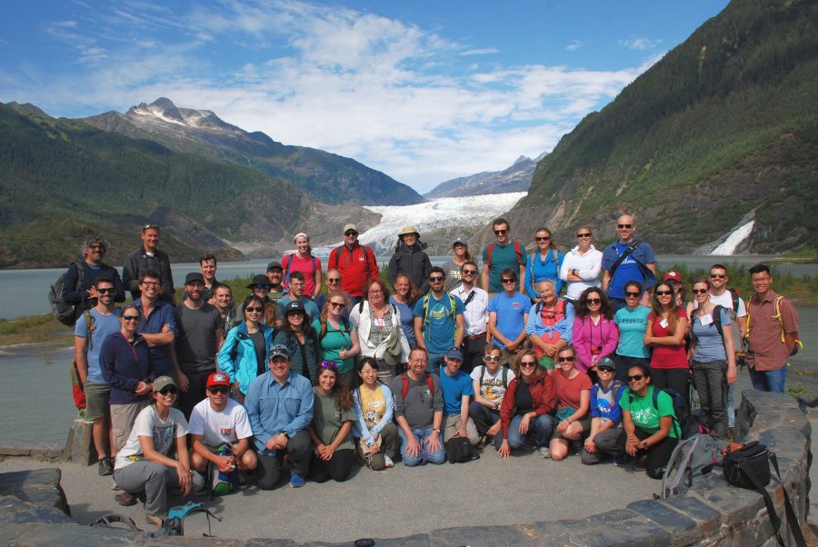 A group of about 50 people smile in a valley with a glacier in the background.