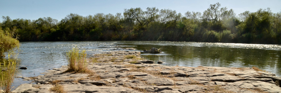 A water-worn sandstone slab protrudes into a river with trees on the far bank.