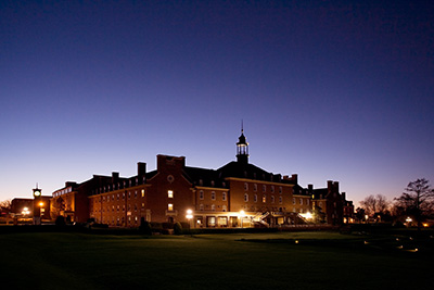 A lit brick building with an expansive lawn glows against a darkening sky.