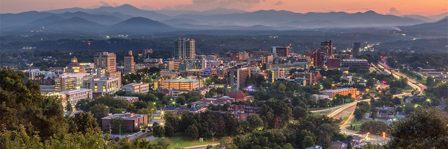 The downtown area of a medium-sized city at dusk among a hilly, treed area.